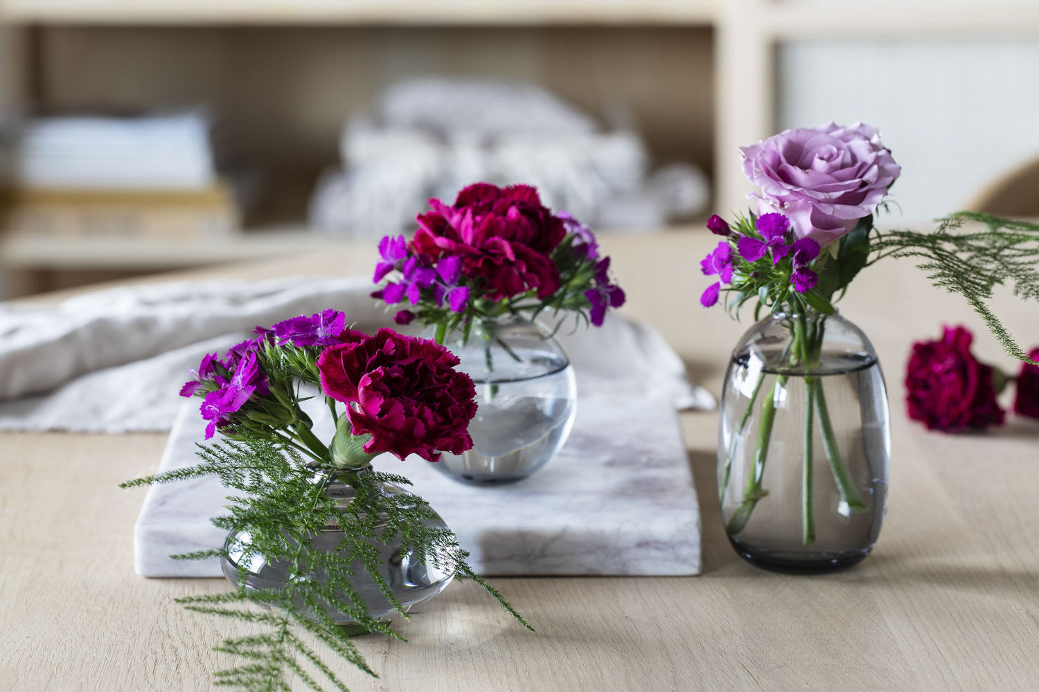 Little bud vases of deep red carnations, sweet william and a lilac rose lined up on a marble board