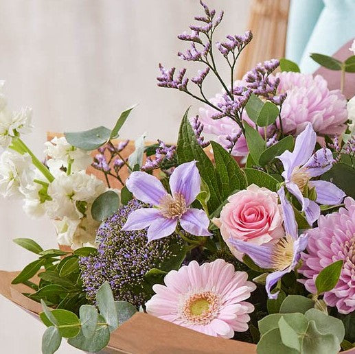 Pastel hand-tied bouquet of pink roses, gerbera and lilac clematis with eucalyptus, wrapped in kraft paper