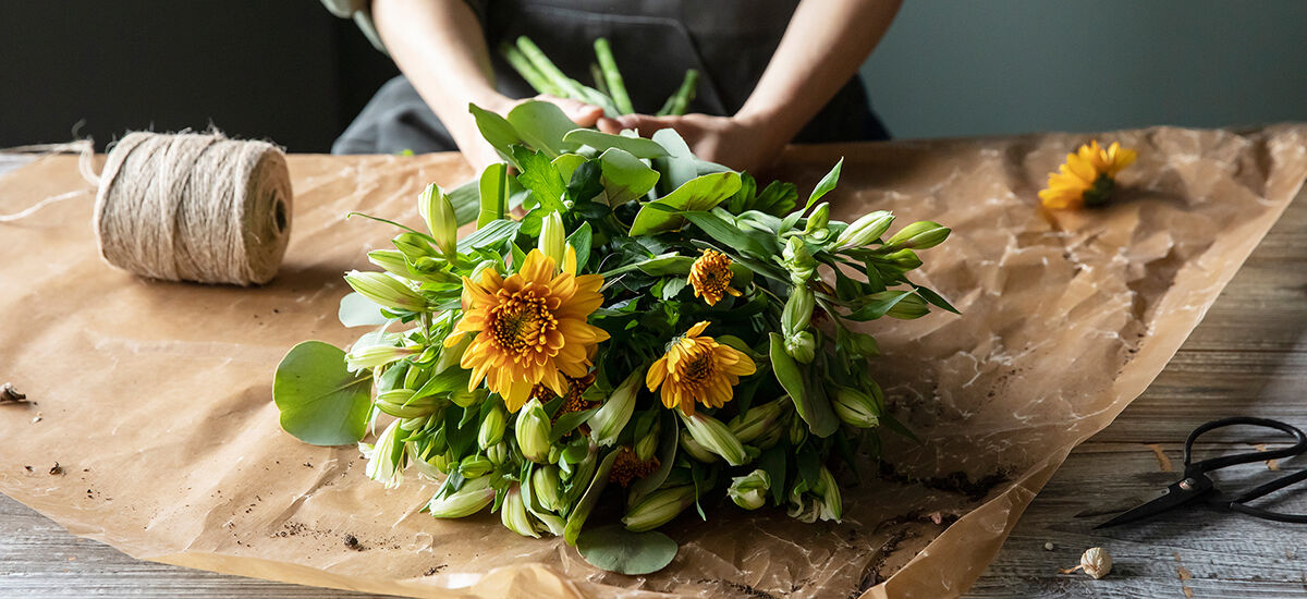 Florist wrapping a bouquet of orange and yellow blooms in kraft paper on the workbench at The Petal Boutique Winchester